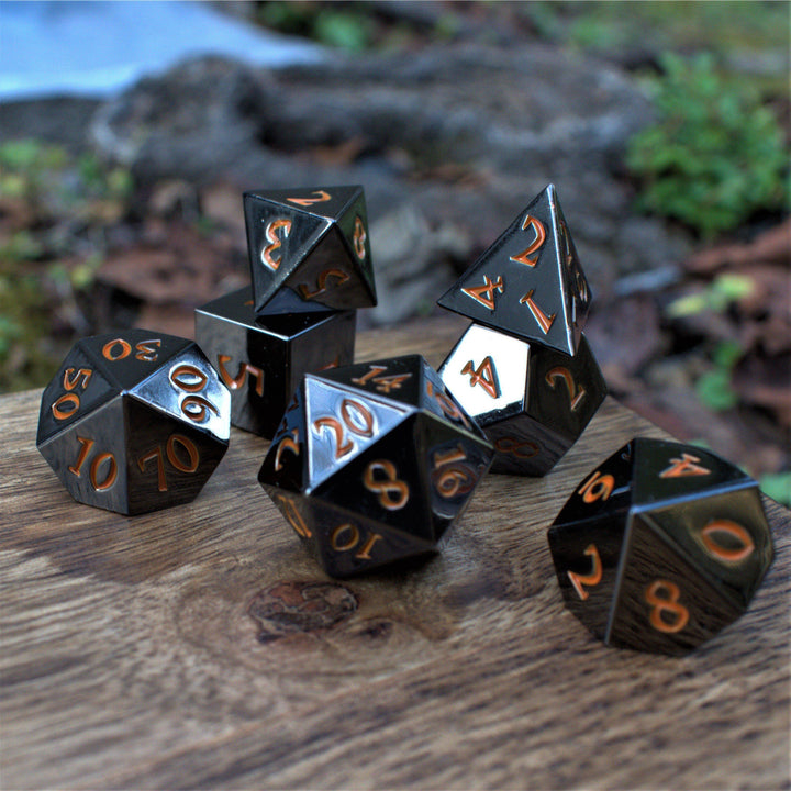 A set of black metal dnd dice with orange numbers, including various shapes such as a d4, d6, d8, d10, d12, and d20, displayed on a wooden surface.