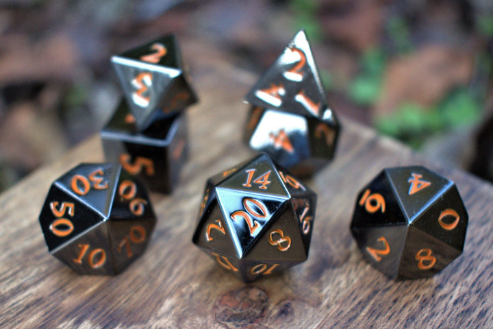 A set of black metal dnd dice with orange numbers, including various shapes such as a d4, d6, d8, d10, d12, and d20, displayed on a wooden surface.