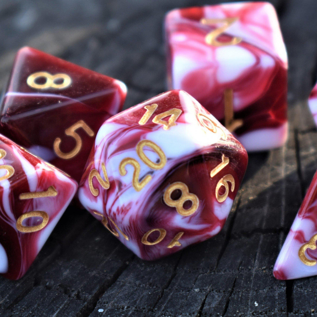A set of acrylic dice with engraved numbers, featuring red and white swirls, on a wooden surface.