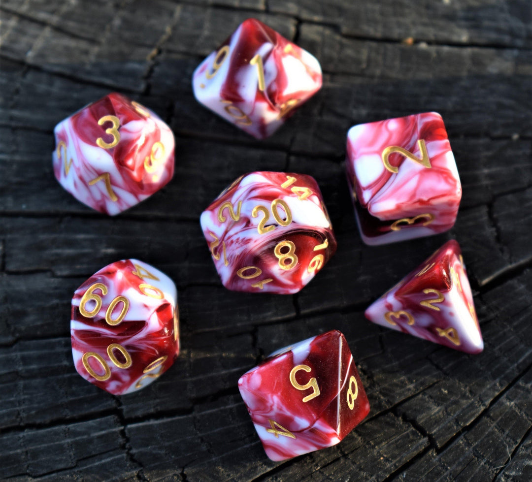 A set of acrylic dice with engraved numbers, featuring red and white swirls, on a wooden surface.