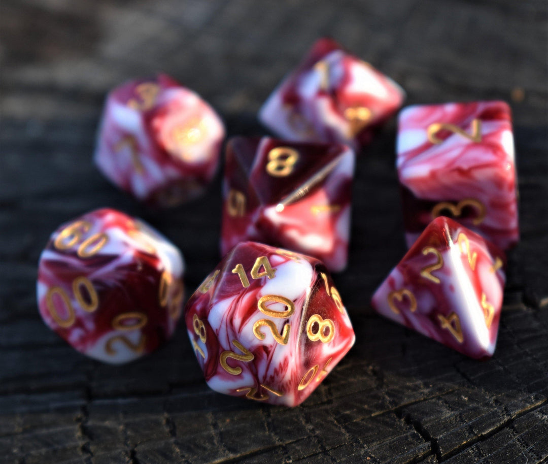 A set of acrylic dice with engraved numbers, featuring red and white swirls, on a wooden surface.
