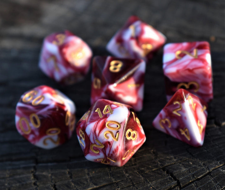 A set of acrylic dice with engraved numbers, featuring red and white swirls, on a wooden surface.