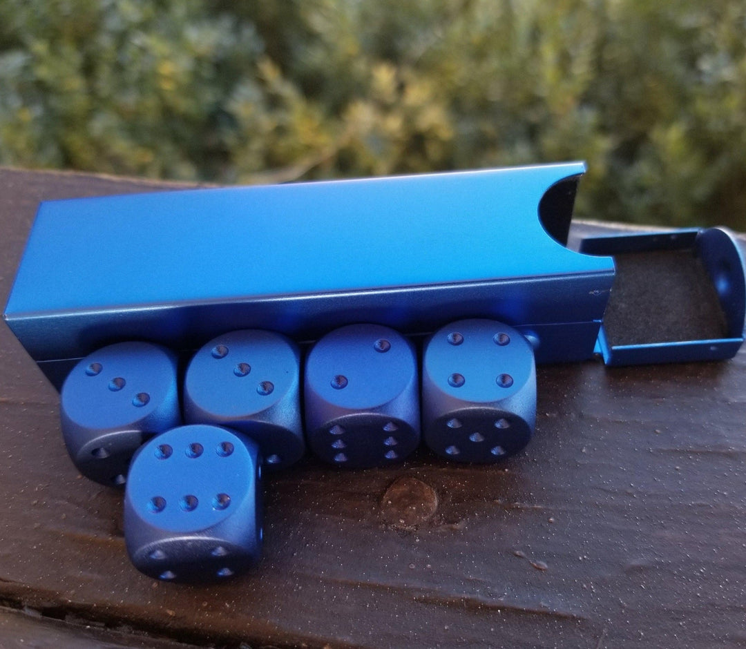 A set of blue aluminum D6 dice with engraved numbers and pips, displayed in front of a foam-lined case.