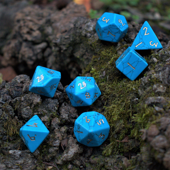 A set of blue turquoise stone dice with engraved numbers placed on a mossy surface.