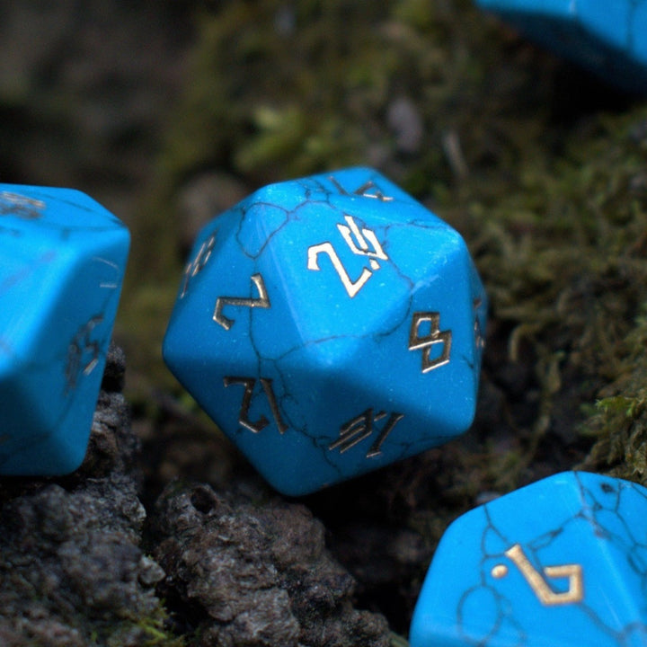 A set of blue turquoise stone dice with engraved numbers placed on a mossy surface.