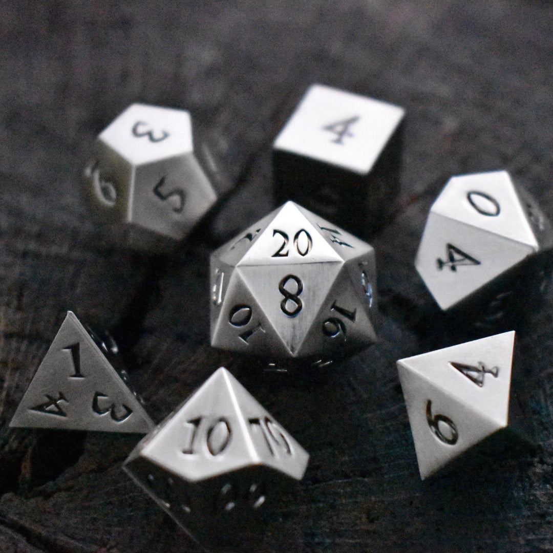 A collection of silver metal dice with engraved numbers, including various shapes such as a d4, d6, d8, d10, d12, and d20.
