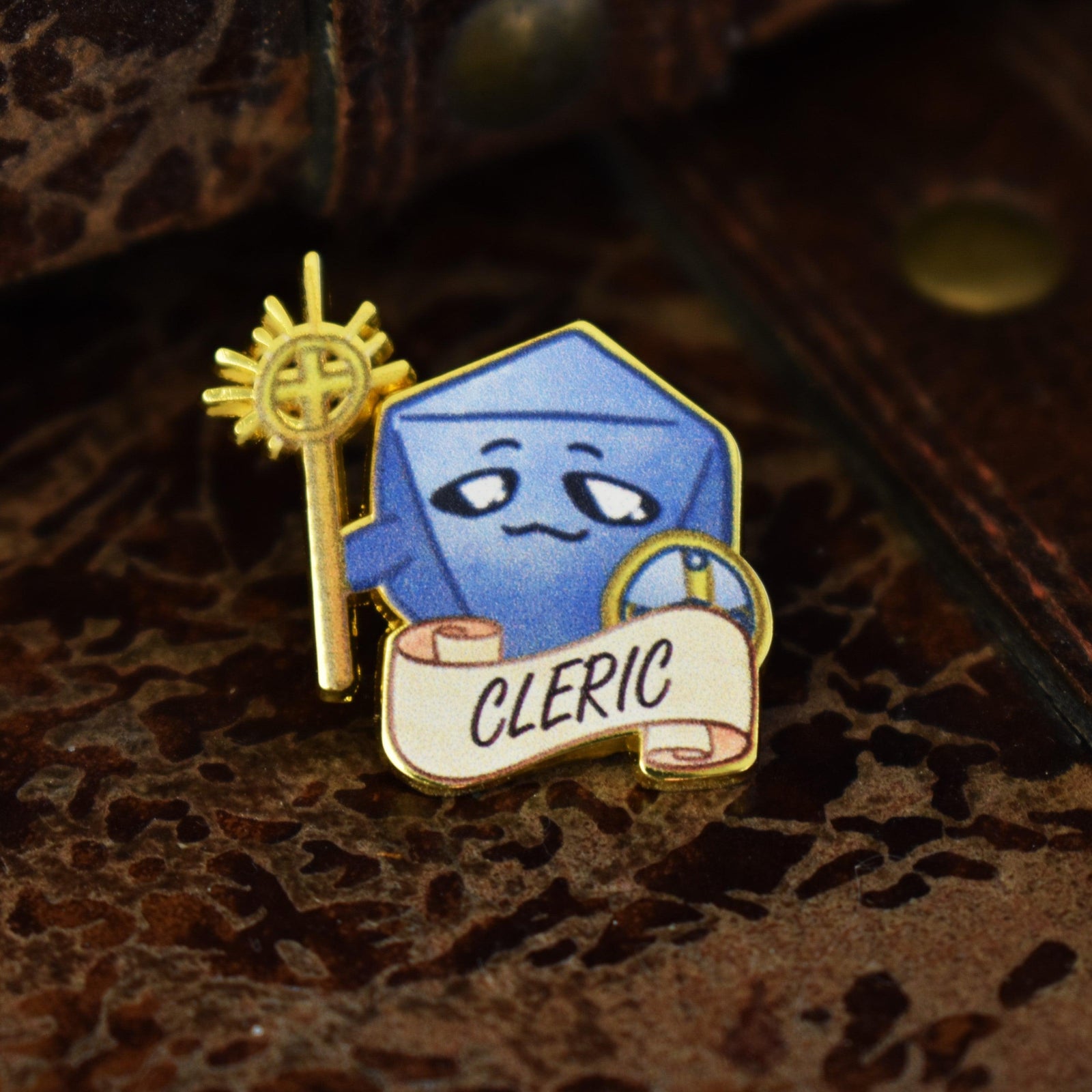 A Cleric class dice pin with a blue enamel finish, gold detailing, and the word 'CLERIC' displayed on a banner.