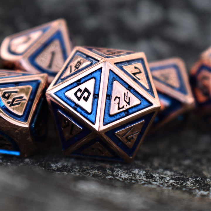 A close-up of a bronze and blue metal dice set with engraved numbers, displaying various dice including a D4, D6, D8, D10, D12, and D20.