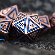 A close-up of a bronze and blue metal dice set with engraved numbers, displaying various dice including a D4, D6, D8, D10, D12, and D20.