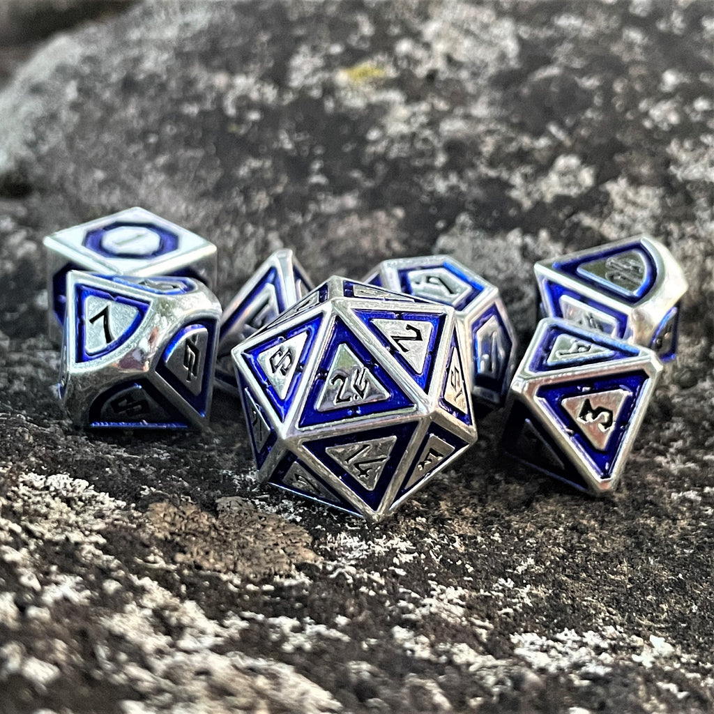 A set of blue and silver metal dnd dice with engraved numbers, placed on a textured stone surface.