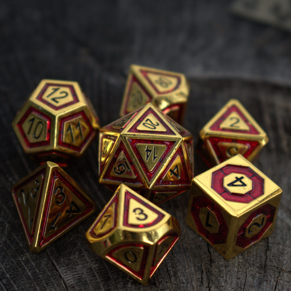A collection of red and gold metal dice with engraved numbers, including various shapes such as a d4, d6, d8, d10, d12, and d20.