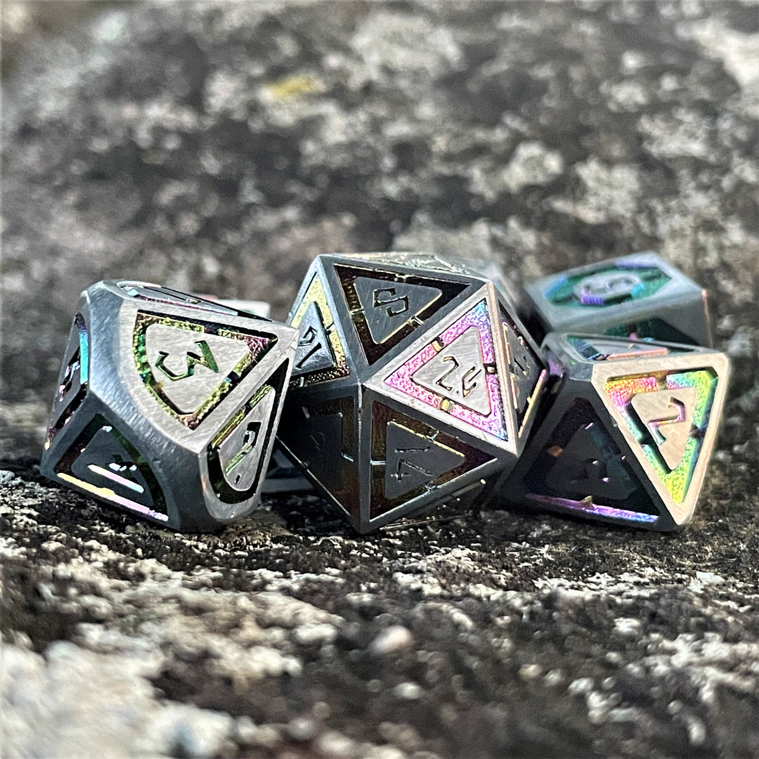 A set of silver metal dnd dice with iridescent properties, including engraved numbers, displayed on a rocky surface.