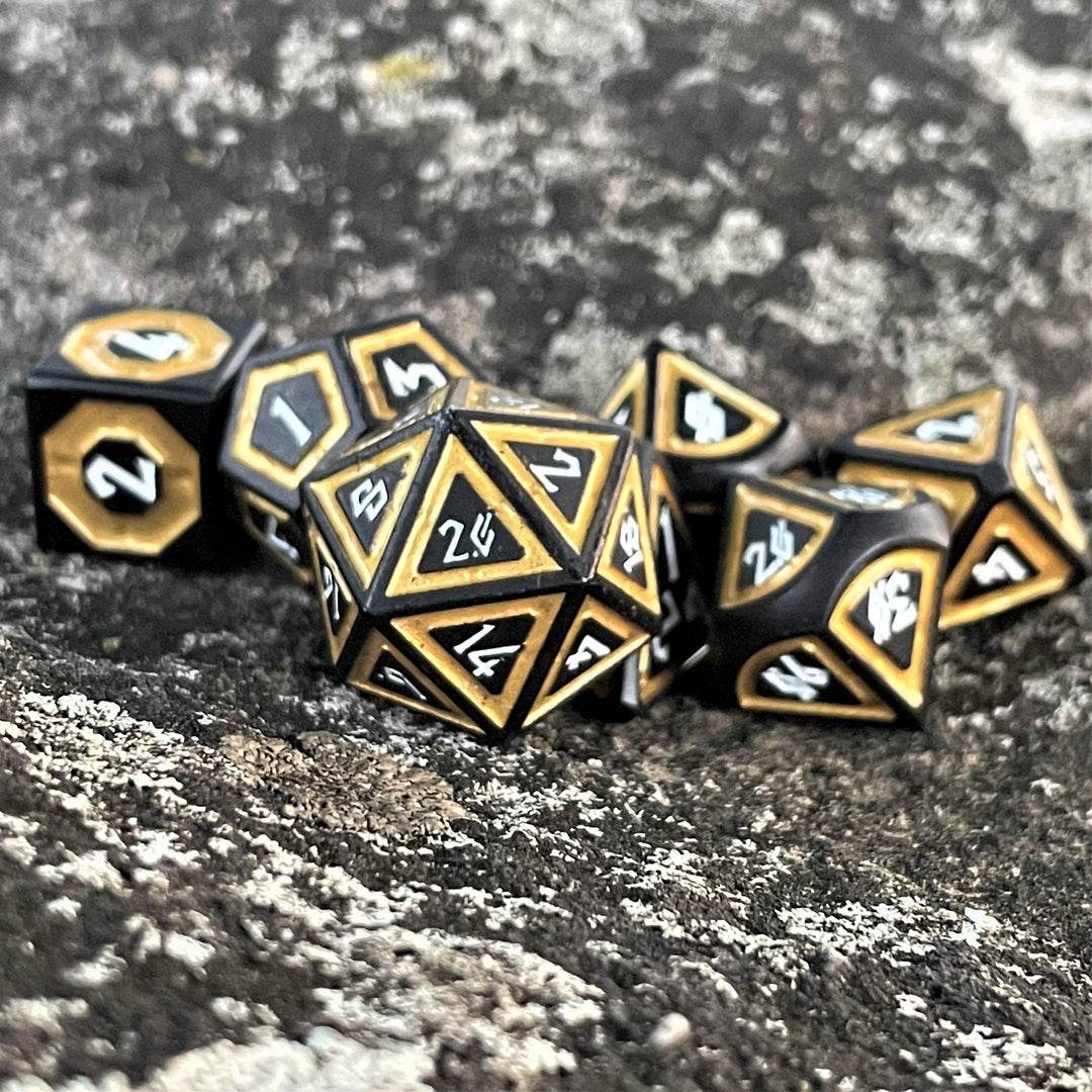 A set of black metal polyhedral dice with thick gold borders on each face and white numbering for wargaming tabletop gaming and board games