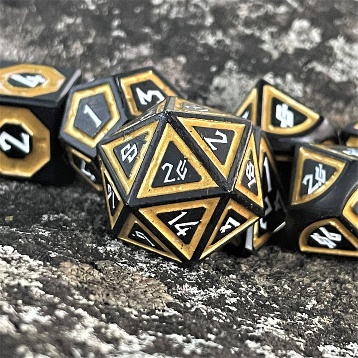 A set of black metal polyhedral dice with thick gold borders on each face and white numbering for wargaming tabletop gaming and board games
