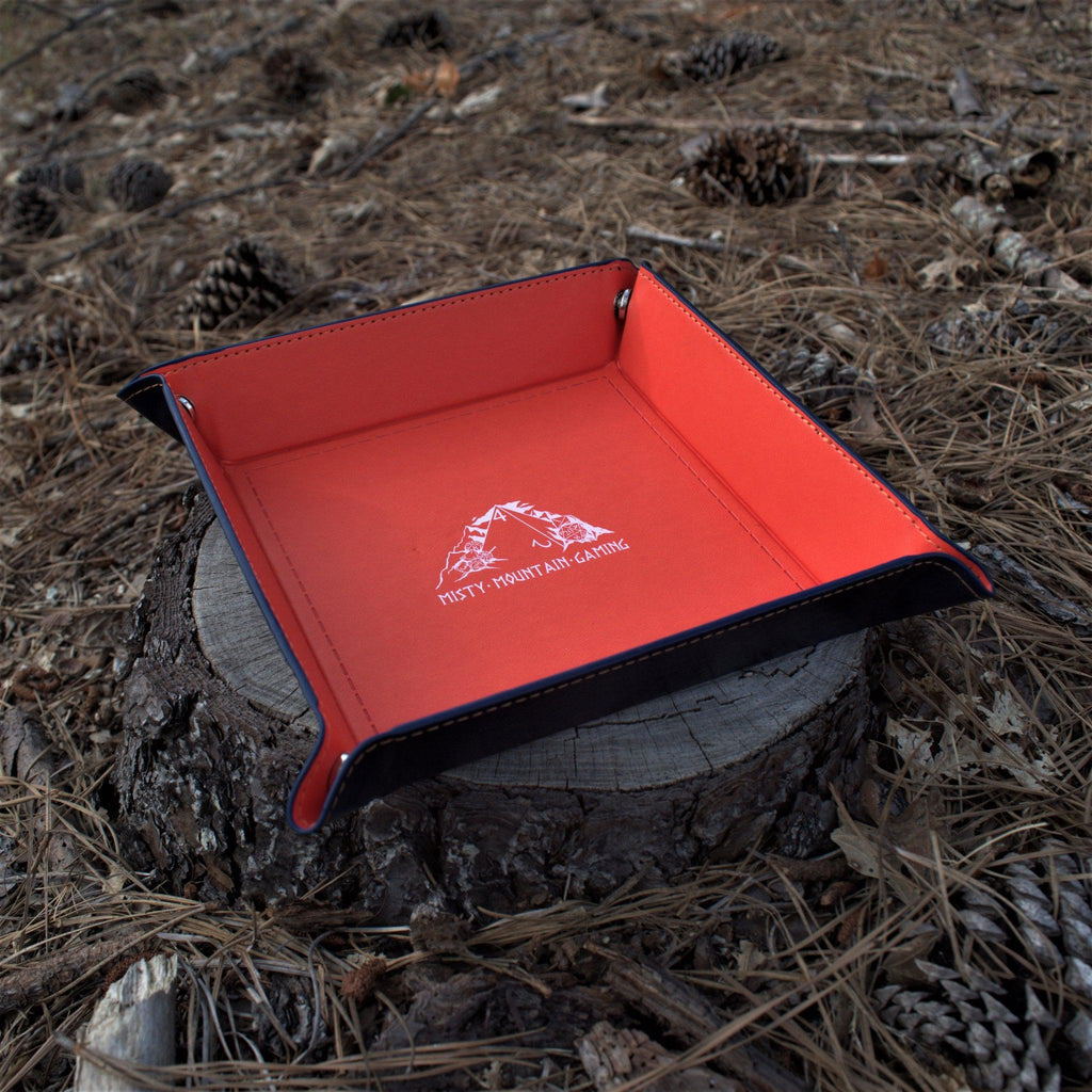 A collapsible dice tray made of poly-leather, featuring the Misty Mountain Gaming logo, placed on a wooden surface.