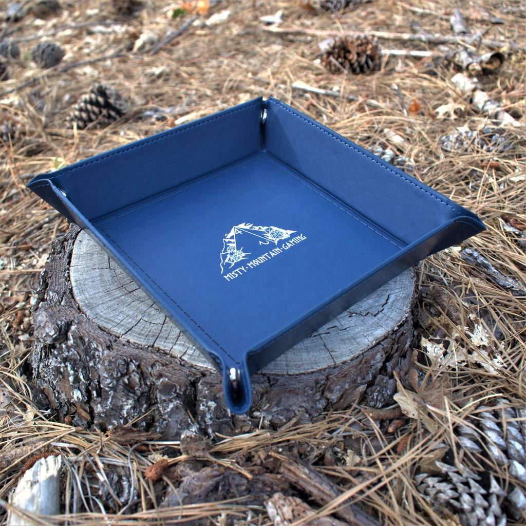 A collapsible dice tray made of poly-leather, featuring the Misty Mountain Gaming logo, placed on a wooden surface.