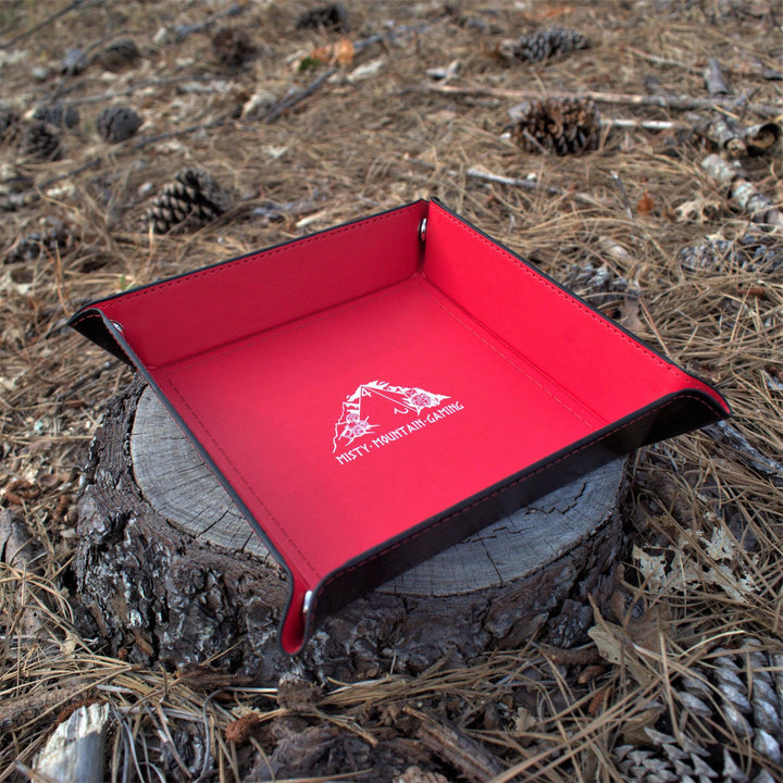 A collapsible dice tray made of poly-leather, featuring the Misty Mountain Gaming logo, placed on a wooden surface.