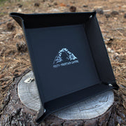 A collapsible dice tray made of poly-leather, featuring the Misty Mountain Gaming logo, placed on a wooden surface.