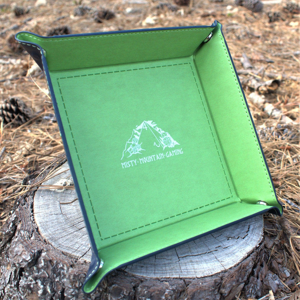 A collapsible dice tray made of poly-leather, featuring the Misty Mountain Gaming logo, placed on a wooden surface.