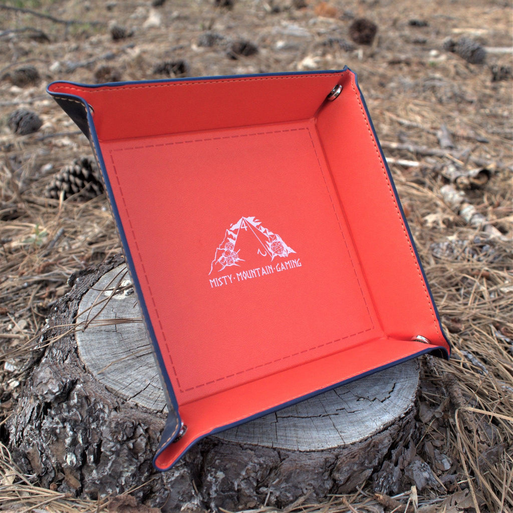 A collapsible dice tray made of poly-leather, featuring the Misty Mountain Gaming logo, placed on a wooden surface.