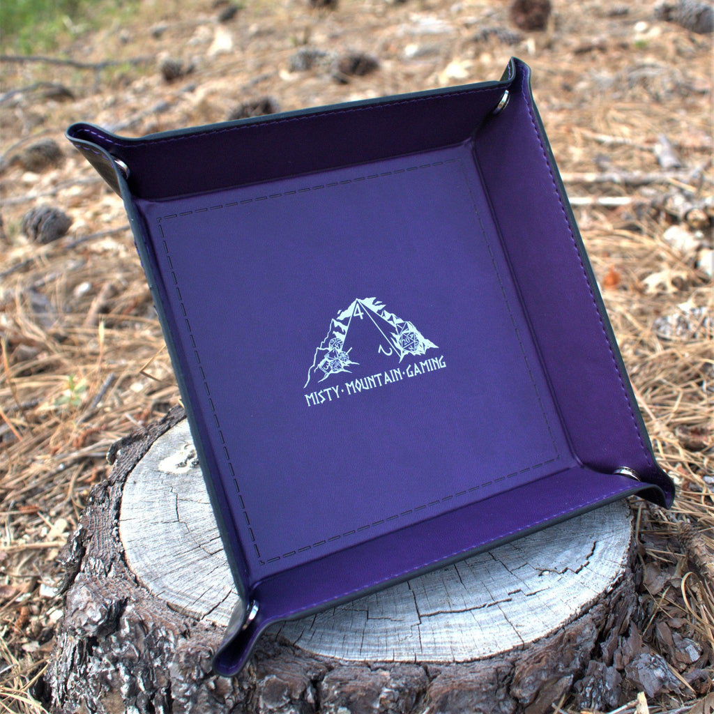 A collapsible dice tray made of poly-leather, featuring the Misty Mountain Gaming logo, placed on a wooden surface.