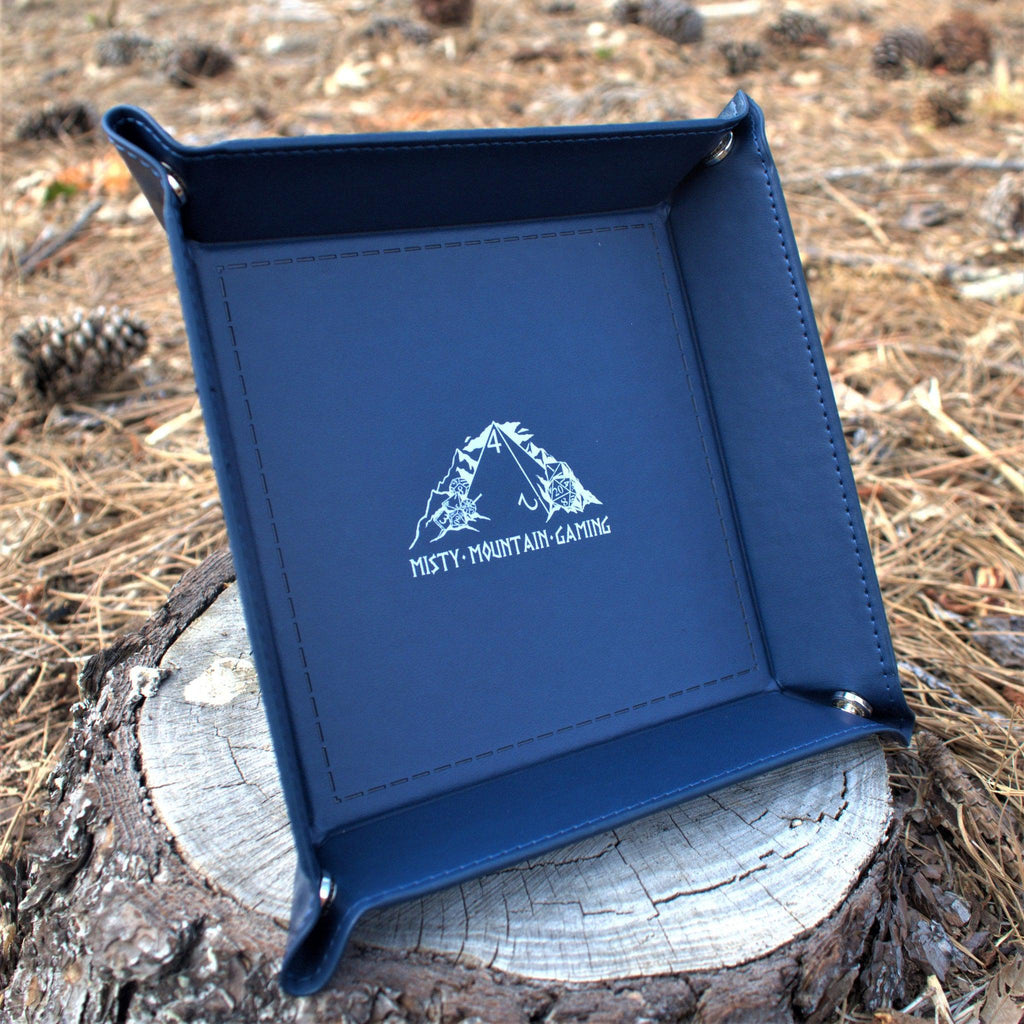 A collapsible dice tray made of poly-leather, featuring the Misty Mountain Gaming logo, placed on a wooden surface.