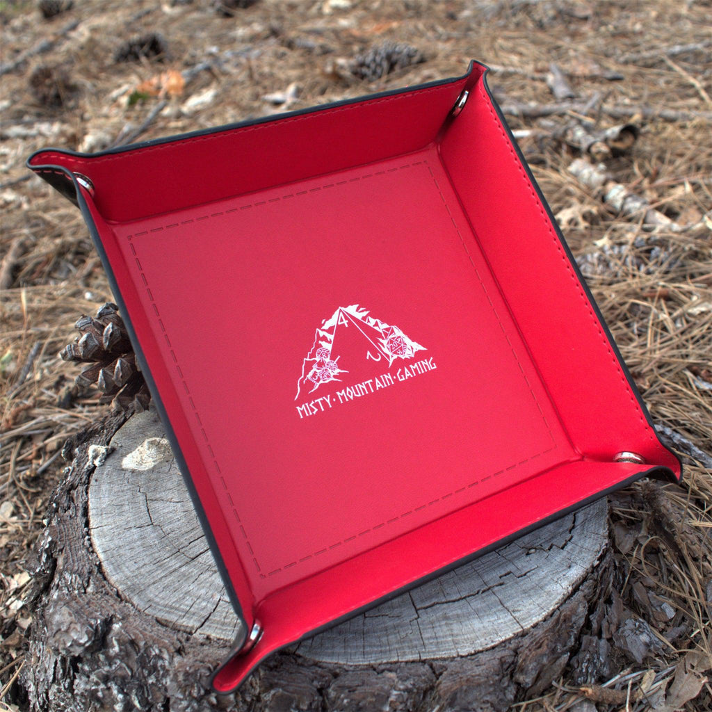 A collapsible dice tray made of poly-leather, featuring the Misty Mountain Gaming logo, placed on a wooden surface.