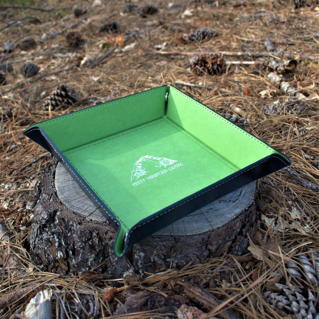 A collapsible dice tray made of poly-leather, featuring the Misty Mountain Gaming logo, placed on a wooden surface.