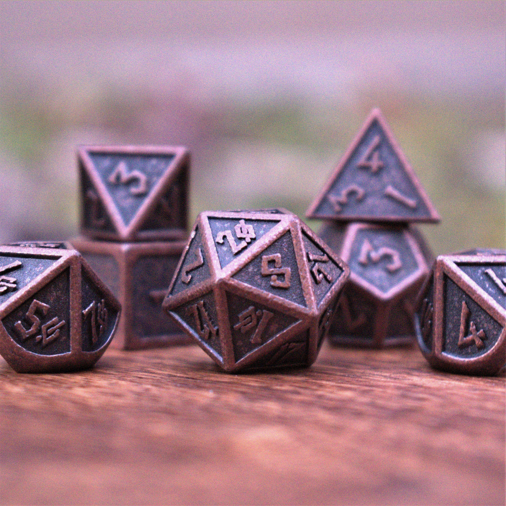 A set of bronze metal dice with embossed numbers, including various shapes such as a d4, d6, d8, d10, d12, and d20, displayed on a wooden surface.