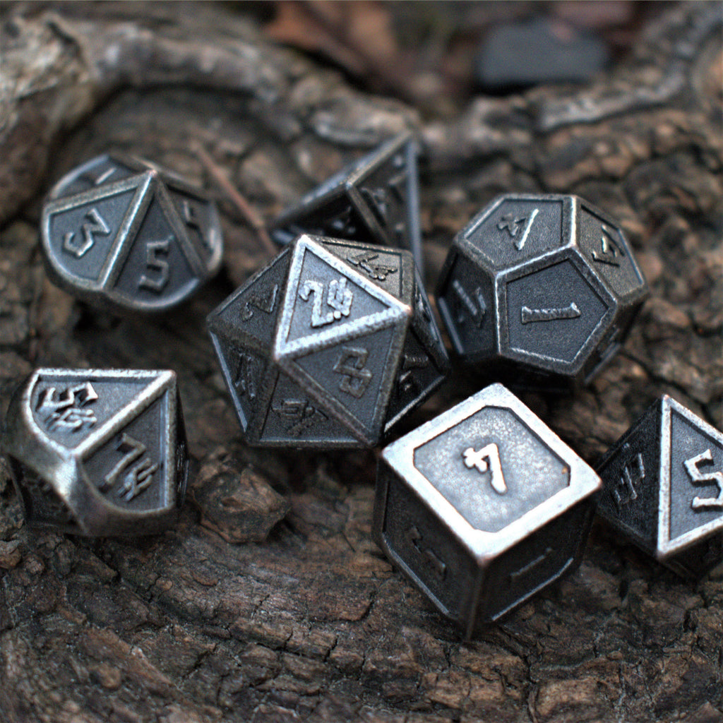 A set of worn silver metal dice with engraved numbers displayed on a wooden surface.
