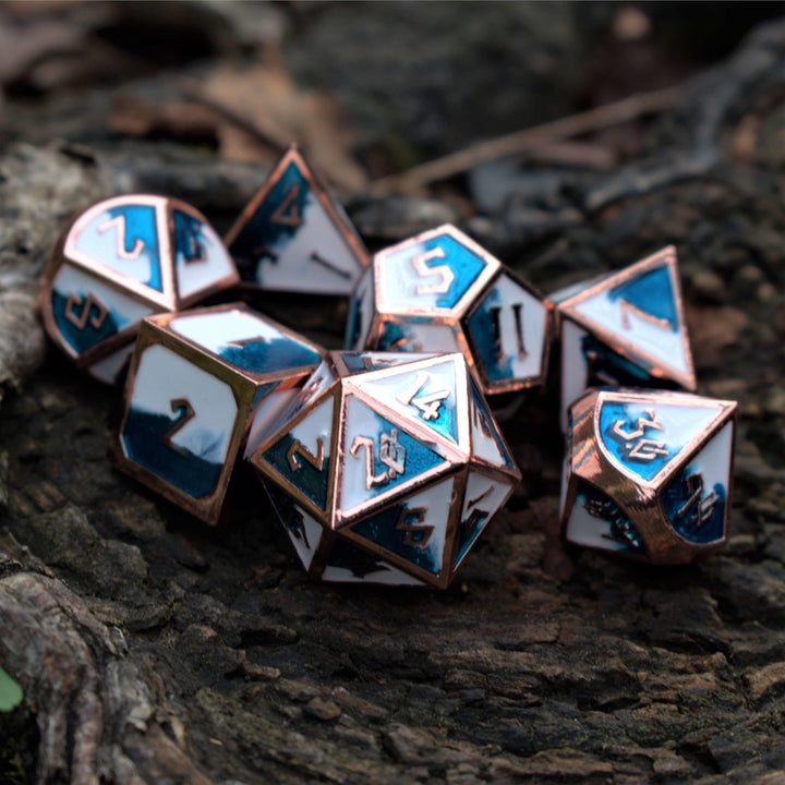 A set of metal dice with embossed numbers, featuring white faces with blue and silver details, scattered on a wooden surface.