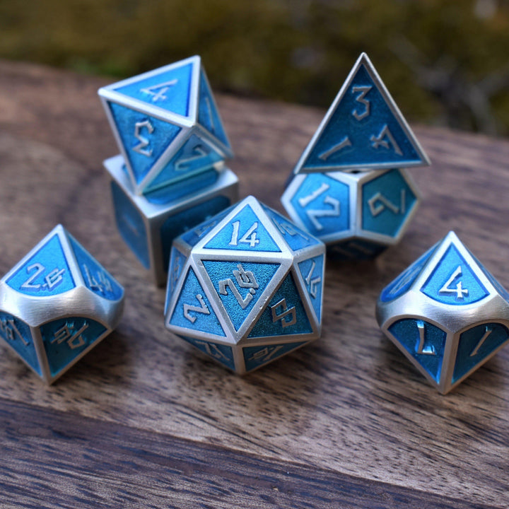 A set of metal dice in blue and silver colors, including various shapes such as a d4, d6, d8, d10, d12, and d20, displayed on a wooden surface.