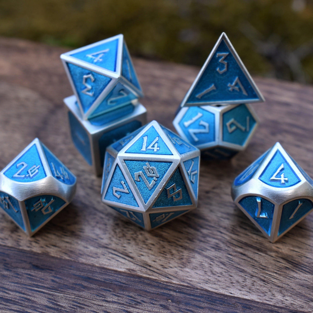 A set of metal dice in blue and silver colors, including various shapes such as a d4, d6, d8, d10, d12, and d20, displayed on a wooden surface.