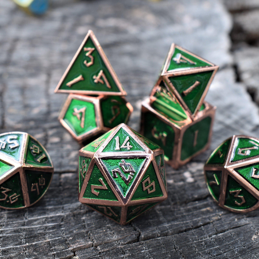 A set of green metal dice with bronze metal edges and embossed numbers, displayed on a wooden surface.