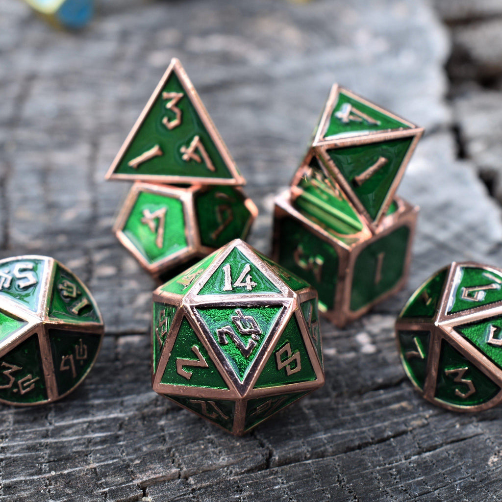 A set of green metal dice with bronze metal edges and embossed numbers, displayed on a wooden surface.