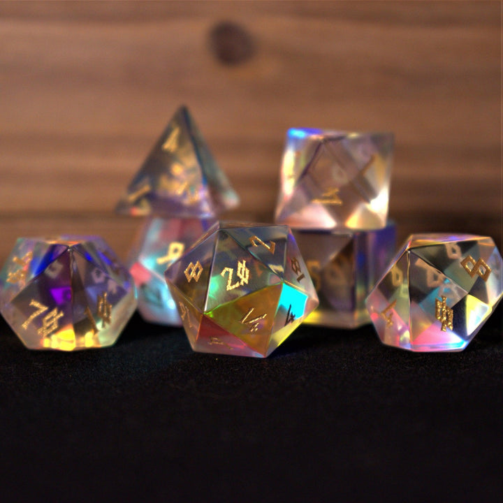 A set of iridescent glass dice with engraved numbers, including various shapes such as a four-sided die (D4), six-sided die (D6), eight-sided die (D8), ten-sided dice (D10), twelve-sided die (D12), and twenty-sided die (D20).