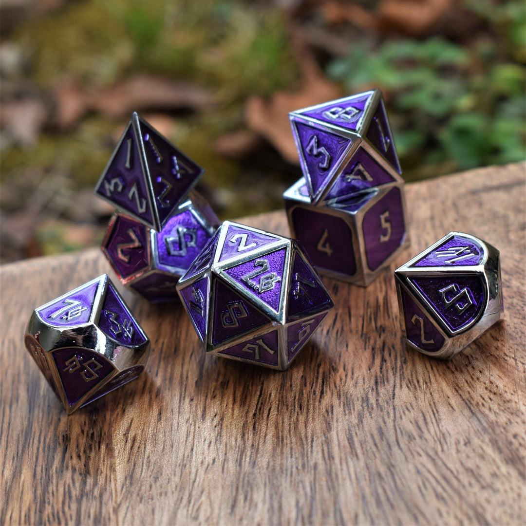 A set of purple and silver metal dice with embossed numbers, including various shapes typical for role-playing games.