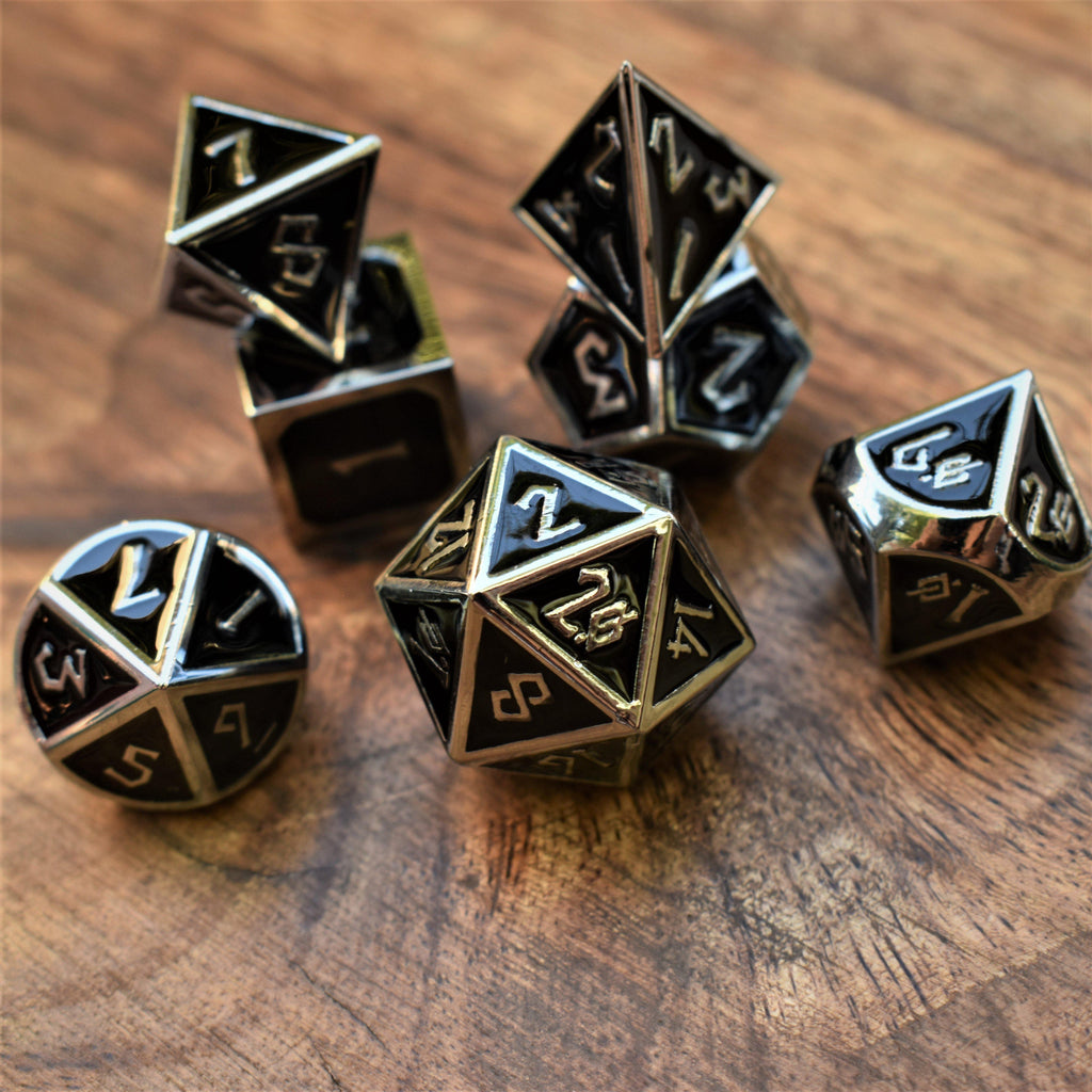 A set of metal dice in silver and black colors, including various shapes such as a d4, d6, d8, d10, d12, and d20, displayed on a wooden surface.