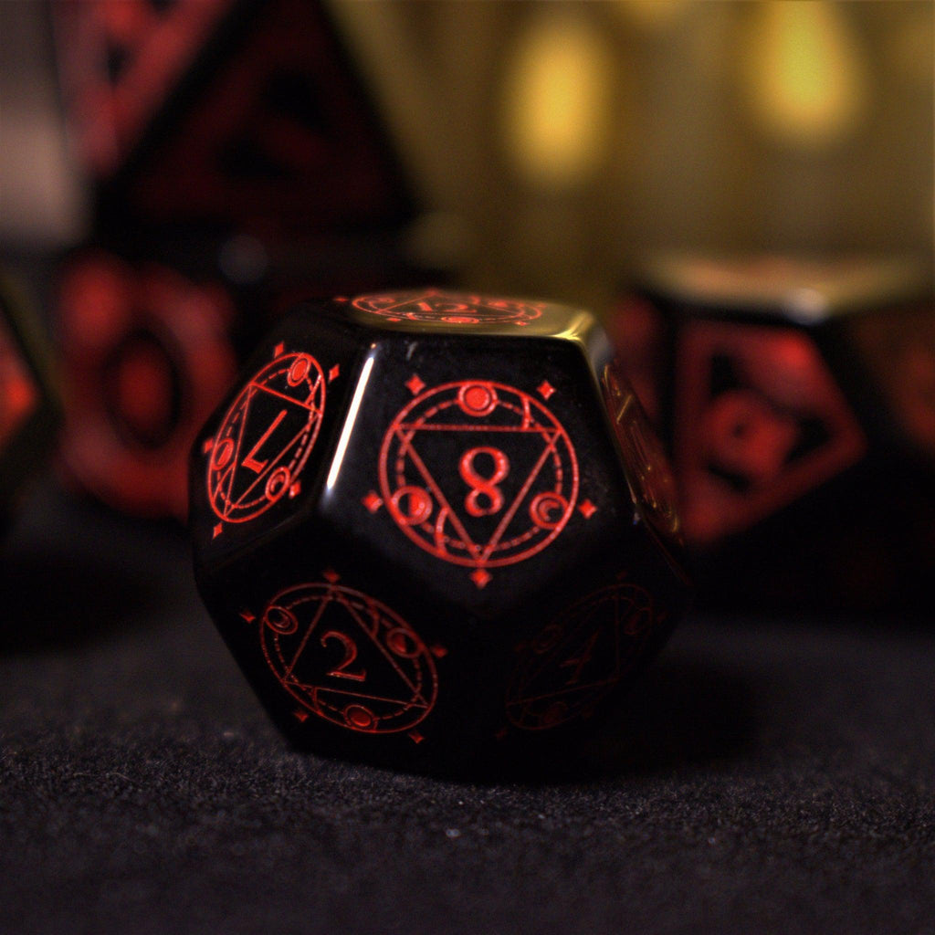 A set of black Obsidian gemstone dice with red engraved numbers and symbols, including a D4, D6, D8, two D10s, D12, and D20, displayed on a dark surface with a blurred light background.