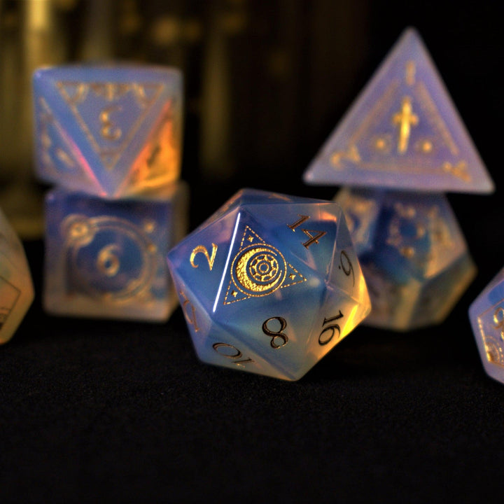 A collection of hand-carved, opalescent white gemstone dnd dice with engraved numbers, displayed on a dark surface.