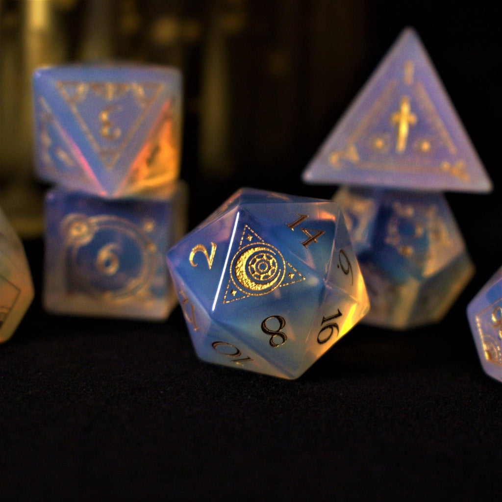 A collection of hand-carved, opalescent white gemstone dnd dice with engraved numbers, displayed on a dark surface.
