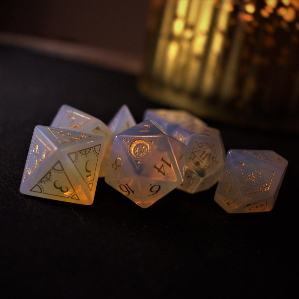 A collection of hand-carved, opalescent white gemstone dnd dice with engraved numbers, displayed on a dark surface.
