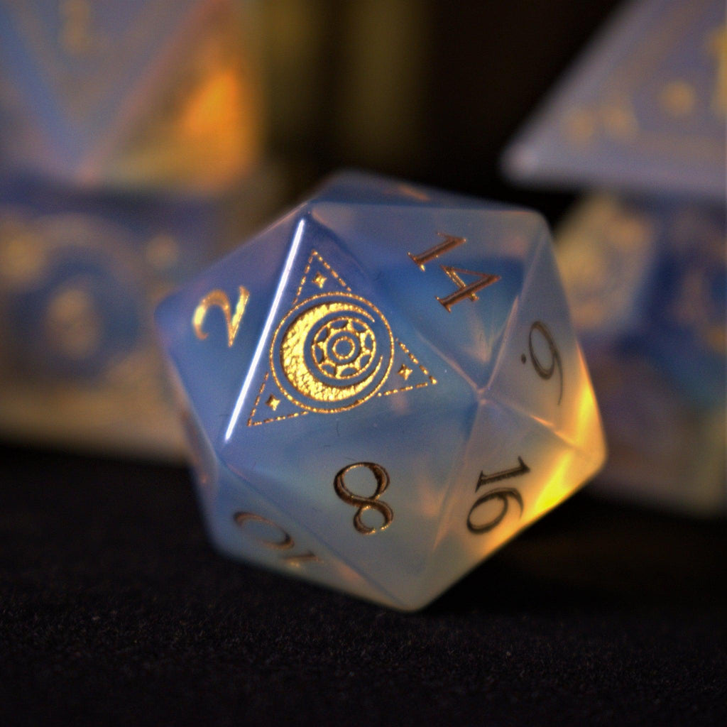 A collection of hand-carved, opalescent white gemstone dnd dice with engraved numbers, displayed on a dark surface.