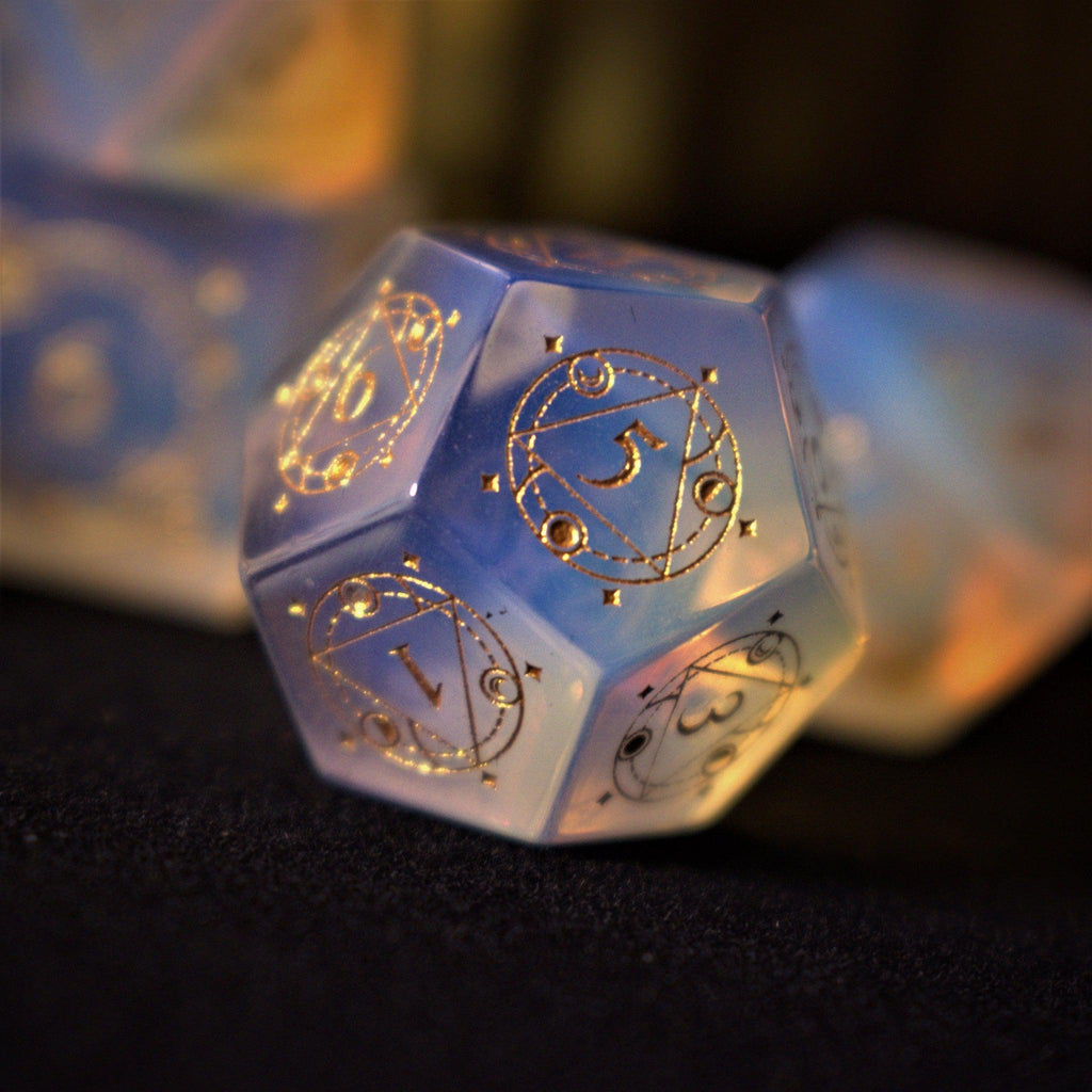 A collection of hand-carved, opalescent white gemstone dnd dice with engraved numbers, displayed on a dark surface.