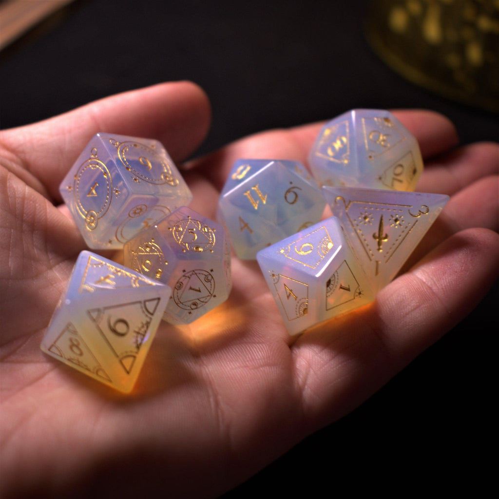 A collection of hand-carved, opalescent white gemstone dnd dice with engraved numbers, displayed on a dark surface.