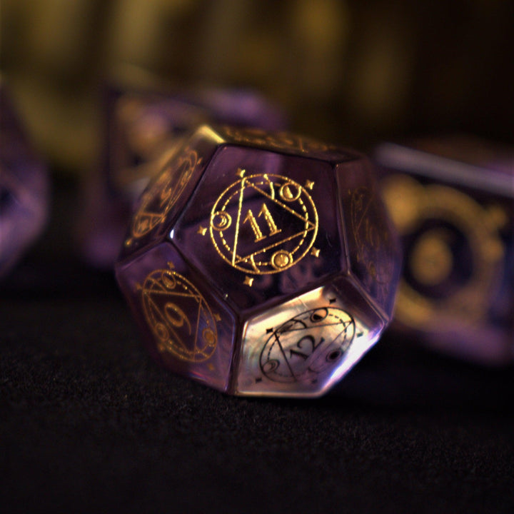 A set of purple glass dice with engraved golden numbers and detail, displayed on a dark surface with a light source in the background creating a reflective sheen on the dice.