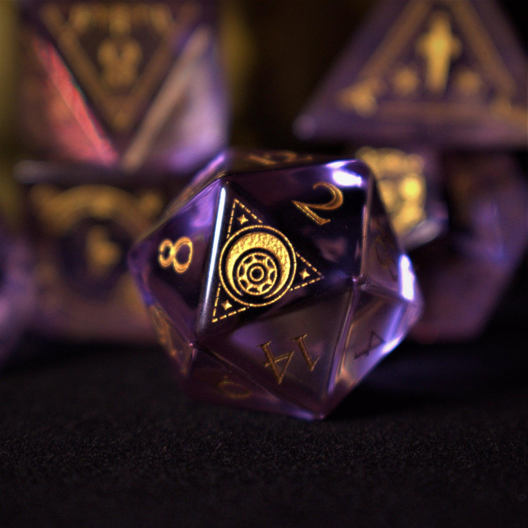 A set of purple glass dice with engraved golden numbers and detail, displayed on a dark surface with a light source in the background creating a reflective sheen on the dice.