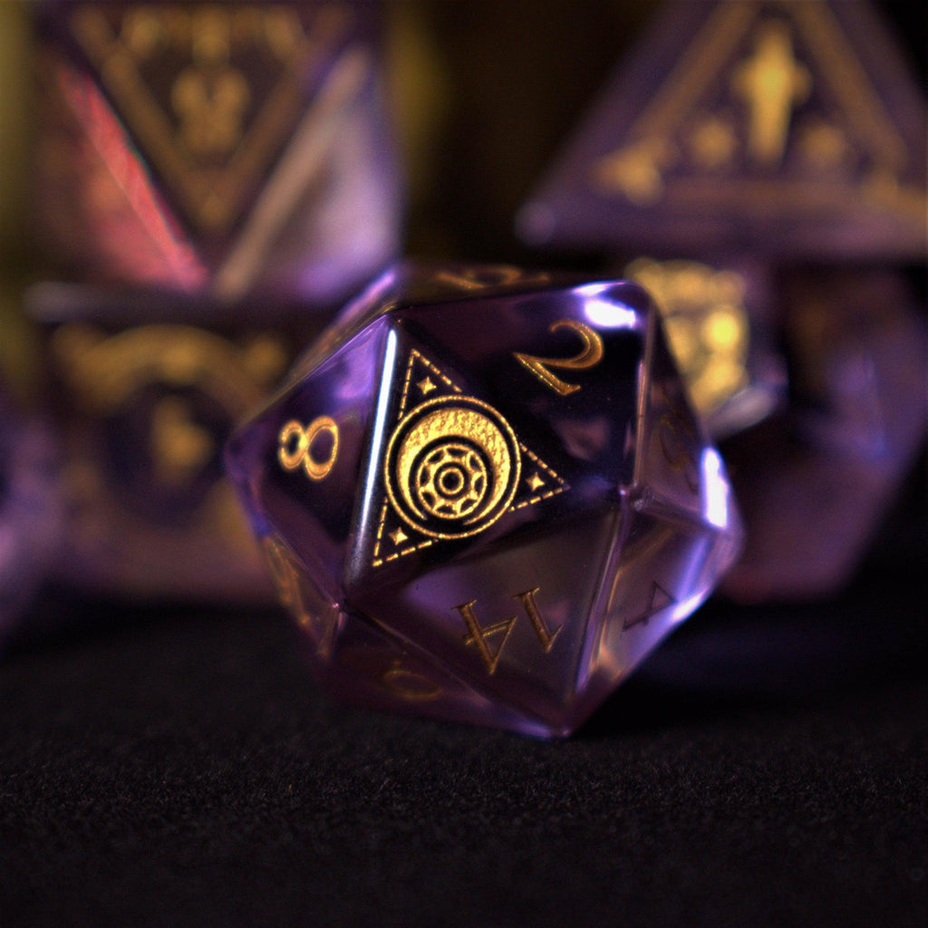 A set of purple glass dice with engraved golden numbers and detail, displayed on a dark surface with a light source in the background creating a reflective sheen on the dice.