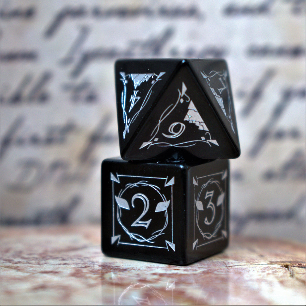 A set of black obsidian stone dnd ttrpg dice with engraved numbers, fangs and fine details, displayed on a textured surface with a blurred background.