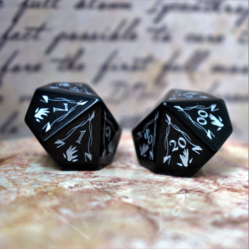 A set of black obsidian stone dnd ttrpg dice with engraved numbers, fangs and fine details, displayed on a textured surface with a blurred background.